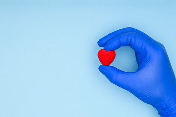 Health insurance or love concept. Hand of a cardiologist in a blue glove holds a red heart. Concept of cardiology and cardiovascular diseases.