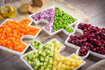 Healthy eating concept. Raw vegetables carrots, peas, onions, cucumber, potatoes, beets cut into cubes lie on plates that are collected in puzzles.