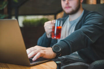 young adult man working on laptop in cafe. drinking fruit tea.