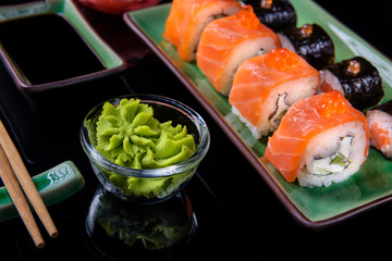 Japanese rolls with spicy wasabi. Set of various rolls of salmon, eel, shrimp and red caviar, in a beautiful green bowl, on a black background with reflection.