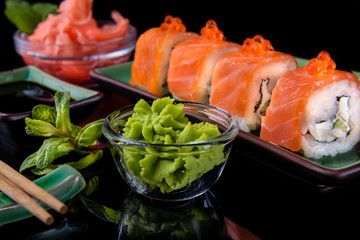 Japanese food. A set of various rolls of salmon, eel, shrimp and red caviar, in a beautiful green bowl, on a black background with reflection.