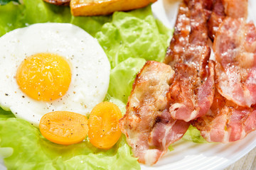 Egg with bacon. Roast potatoes. French fries and egg with bacon on top in a white bowl, on a large table with greens.