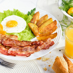 Egg with bacon. Fried bacon with French fries and tender egg, and a glass of fresh juice.