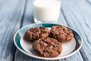 A cup of milk and a plate of chocolate cookies on blue wooden floor