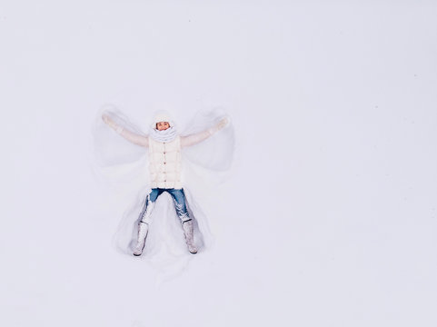 Top view aerial drone. Snow angel. Young girl lying snowdrift, waving his hands different directions