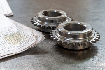 Two gears lie on a testing table with technical drawings.