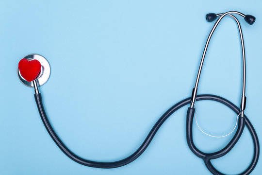 Stethoscope and decorative red heart on a blue photo of a doctor in general. Closeup of a red heart and a stethoscope on a blue background. Heart and statoscope closeup on blue background, top view.