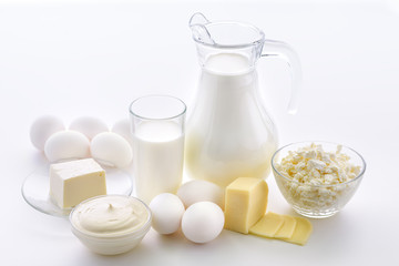 Milk composition with a jug and a glass of milk with cheese and eggs next to a plate of cottage cheese and sour cream on a white background.