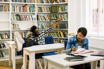 Beautiful African-American students work in the library. The girl smiles and working with the...