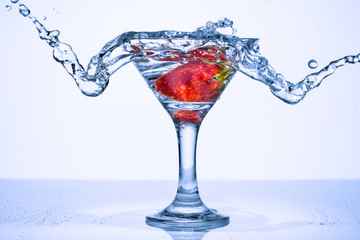 Splash in a glass. Frozen splashes of clean, spring water, in a glass with frozen strawberries, on a white background.