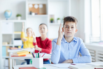 Clever youthful pupil raising hand to answer question of teacher during check-up of home assignment
