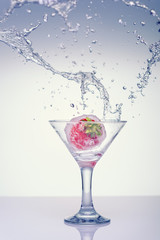 Splash in a glass with strawberries. Frozen splashes of clean, spring water, in a glass with frozen strawberries, on a white background.