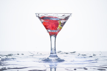 Splash in a glass. Frozen explosion of freshness from water, in a cocktail glass with strawberries. White background.