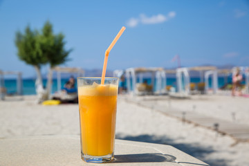 Glass of orange juice on white beach sea view coast background. Relax and vacation concept.