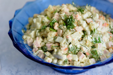 Russian salad with olive mayonnaise in a blue plate, on a white tablecloth.