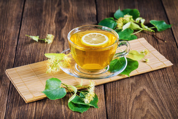 A cup of tea, standing on a wooden table, surrounded by fragrant linden flowers, in the rays of sunlight.