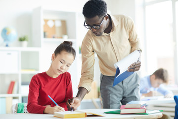 African-american teacher pointing at notes of schoolgirl while explaining her how to correct mistake