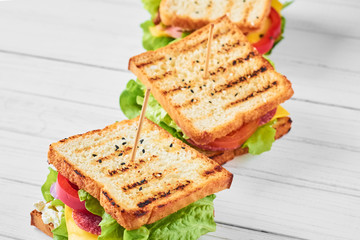Three sandwiches with ham, lettuce and fresh vegetables on a white background