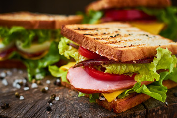 Homemade sandwich with ham, lettuce, cheese and tomato on a wooden background