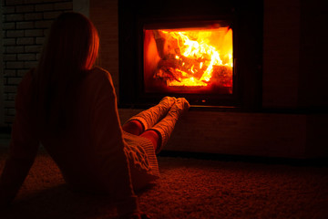 A woman in knitted socks is sitting near the fireplace on a cold winter evening.