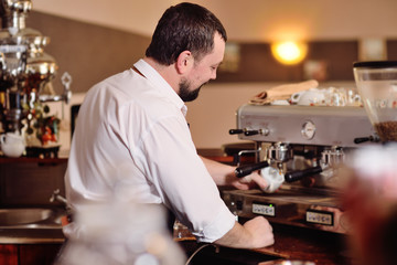 portrait of a handsome bearded barista preparing coffee on the background of a coffee shop and a coffee machine