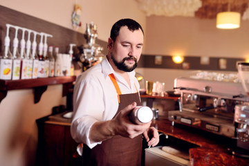 portrait of a handsome bearded barista preparing coffee on the background of a coffee shop and a coffee machine