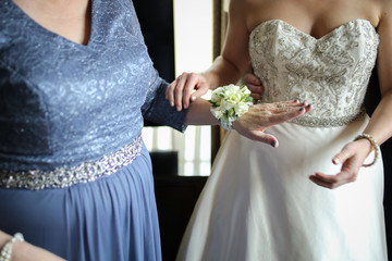 Bride Putting a White Floral Corsage on the Mother of the Bride Wearing an Ornate Wedding Gown