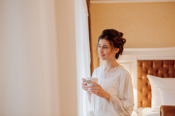 the bride is drinking coffee, bride holds a cup of coffee, bride in a white coat, morning of the...