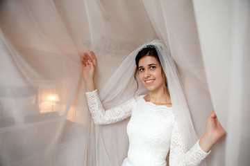 Bride morning preparation. Beautiful bride in white wedding negligee near bedroom window
