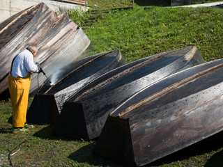 elderly man  cleaning wooden boats after the season with a high pressure cleaner