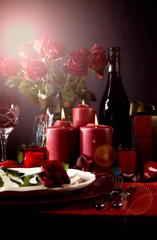 Romantic Valentine's Day Table Setting for two with red roses, gift and burning candles against a black background with lens flare.