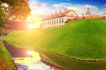 Naklejka premium Pond with a forest and hill with castle buildings against sky with sunset