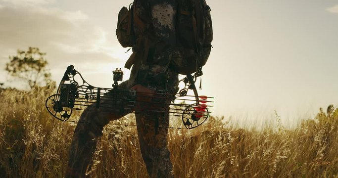 Bowhunter walking through golden grass at sunset