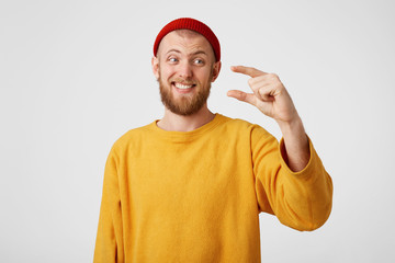 Handsome unshaved male shows something tiny with hands, looking haughtily on it, dressed in yellow...