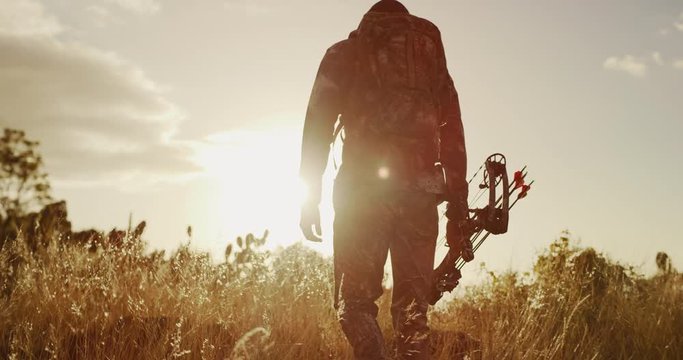 Bowhunter walking through golden grass into the sunset