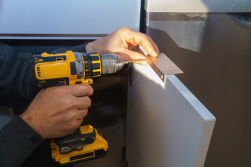 Worker sets a new handle on the white cabinet with a screwdriver installing kitchen cabinets