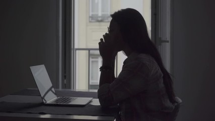 Silhouette of tired young woman with headache working with laptop. Side view of tired businesswoman working on project at home. Overwork concept - Powered by Adobe
