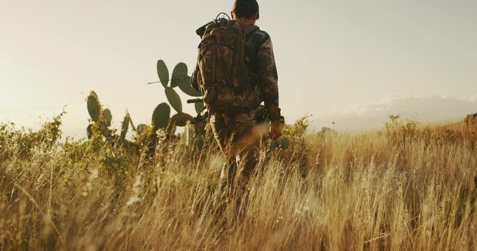 Low angle shot of bowhunter walking through golden grass with an arrow knocked