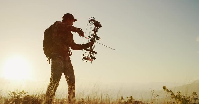 Bowhunter drawing back an arrow at sunset