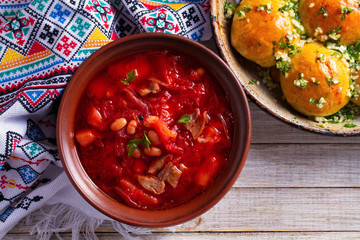 Soup borscht made with vegetables, meat, bean and beet root. Buns Pampushky - Ukrainian garlic bread. Bread rolls with garlic and parsley in baking dish. View from above, top studio shot, horizontal