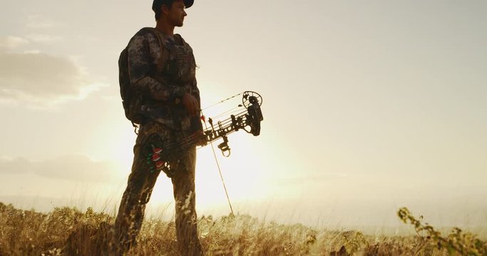 Full orbit shot of hunter standing at sunset with arrow knocked