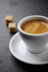 Cup of coffee and two brown sugar cubes on black stone background. Close up. 