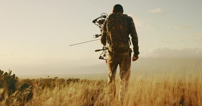 Bowhunter walks through golden grass with an arrow knocked
