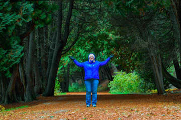 Woman looking at camera, arms wide, standing among cedar trees on Mackinac Island