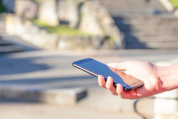 Black smartphone in hand in the park in the open air, lit by the sun