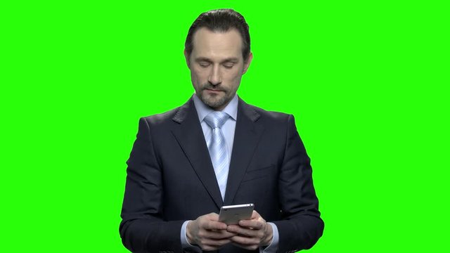 Confident mature man in black suit typing on smartphone. Middle-aged businessman texting message. Green screen hromakey background for keying.