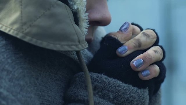 Miserable homeless woman in dirty closes warming her frozen hands, poverty