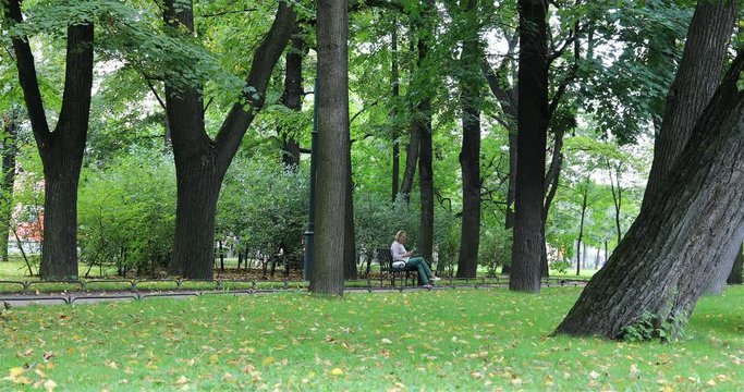 a woman sits on a bench in the park and reads a book.