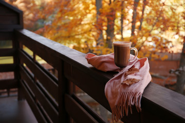 Hot cozy drink and warm scarf on wooden railing at balcony. Space for text