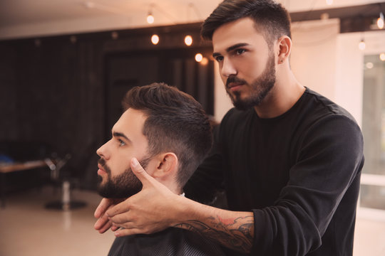 Hairdresser applying serum onto client's beard in barbershop. Professional shaving service